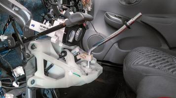 interior or dashboard of a car that is being disassembled or repaired, the steering column frame, shift lever, and interior cables are visible photo