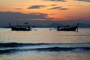 Two silhouette of longtail boat on sea and wave with orange sky and cloud background at Krabi, Thailand. Landscape of ocean at sunset time. photo