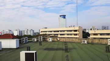 Many kind of air compressors installed on rooftop of terrace with height building, telecommunication tower, blue sky and clouds background. Technology and Exterior design. photo