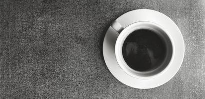 Top view of white cup of black coffee on brown rug or carpet background with copy space in black and white tone. Flat lay of hot drinking on cotton floor wallpaper in monochrome style. photo