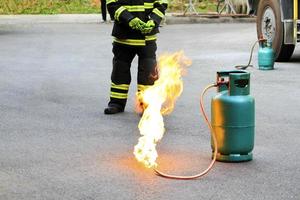 fuego ardiendo en un contenedor de gas verde y bombero o bombero con uniforme de seguridad negro y verde o traje y extinguir el fuego en la calle con fondo de rueda de camión y espacio para copiar. conflagración y riesgo. foto