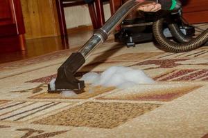 The process of cleaning the carpet with a vacuum cleaner with a water filter. A woman collects the remains of cleaning foam from the dirty surface of the carpet photo