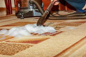 The process of cleaning the carpet with a vacuum cleaner with a water filter. A woman collects the remains of cleaning foam from the dirty surface of the carpet photo