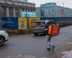 Dnepropetrovsk, Ukraine - 02.10.2022 A delivery service courier with a thermal bag walks through the city. Home food delivery. photo