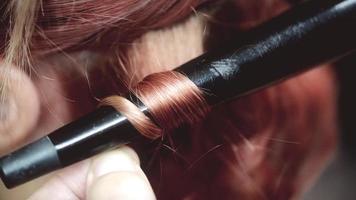 Close-up of a male hairdresser making curls at copper hair with curling irons. video