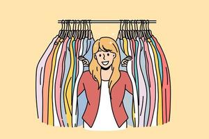 Clothes seller and fashion concept. Young smiling woman cartoon character standing and looking to camera with colorful clothes on hangers both sides vector illustration