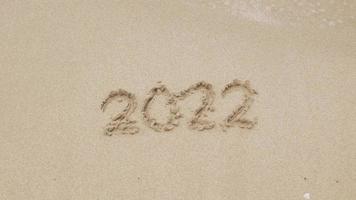 2022 hand skriva siffror på sandig strand för Lycklig ny år 2023, de hav Vinka tvättar bort siffra hand skriven på de gyllene strand sand hav. Bra Hejdå 2022 video