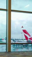 vista interior de lapso de tiempo vertical dentro de la sala de la terminal de salida con ventana gigante con aviones qantas airbus a330 y aviones de otras aerolíneas estacionados en el aeropuerto video