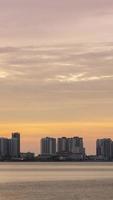 vertical timelapse silhouette view of waterfront city with highrise skyscraper building near sea coast beach while sunset sundown time with vanilla twilight sky video