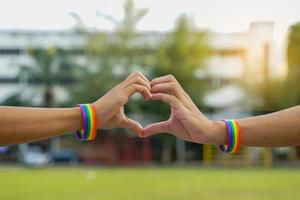 A young Asian Lgbt couple wearing rainbow wristbands put their hands together in a heart shape. to show love Pride of being LGBT. soft and selective focus. photo