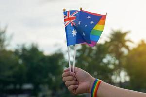 la bandera del arco iris y la bandera nacional de australia la sostienen en manos de personas lgbt que usan pulseras del arco iris. enfoque suave y selectivo. foto