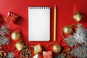 Notepad and pencil for writing wishes and gifts for the New Year and Christmas around the Christmas tree decorations on a red background. photo