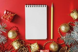 Notepad and pencil for writing wishes and gifts for the New Year and Christmas around the Christmas tree decorations on a red background. photo