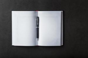 An open Notebook with a black pen on a black background. photo