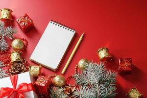 bloc de notas y lápiz para escribir deseos y regalos para el nuevo año y navidad alrededor de las decoraciones del árbol de navidad sobre un fondo rojo. foto