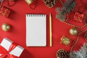 Notepad and pencil for writing wishes and gifts for the New Year and Christmas around the Christmas tree decorations on a red background. photo