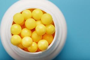 Vitamins of yellow color in the form of round dragees in a white jar on a blue background. photo