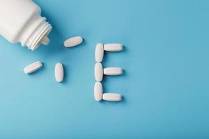 Vitamin E pills fell out of a white jar on a blue background. The letter E is an inscription. photo