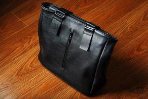 Handmade black leather bag on a wooden background, made of natural material. photo