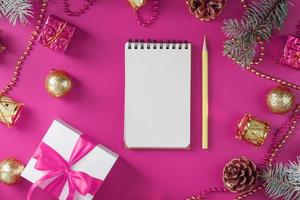 Clean white notepad with pencil around Christmas decorations on pink background. Planning photo