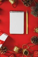 Christmas composition with notepad and a pencil for writing wishes with Christmas tree decorations on a red background. photo