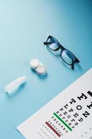 Glasses with Contact Lenses, drops and an Optometrist's Eye Test Chart On a Blue Background. photo