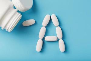 White capsules with vitamins in the form A are poured out of a jar on a blue background. photo