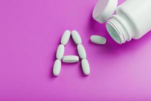 Vitamin A pills fell out of a white jar on a pink background. photo