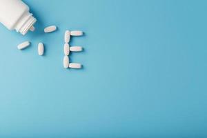 Vitamin E pills fell out of a white jar on a blue background. The letter E is an inscription. photo