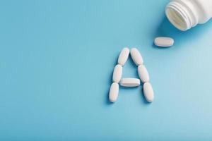 The letter of vitamin A in capsules pour out from the jar on a blue background. photo