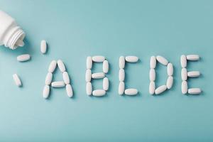 Pour the letter of vitamin A B C D E in capsules from a jar on a blue background photo