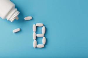 Vitamin B pills fell out of a white jar on a blue background. The letter In the inscription. photo