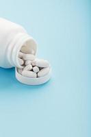 White capsules with vitamins and minerals in the form are poured from a jar on a blue background. photo