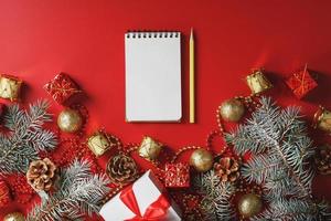 composición navideña con bloc de notas y un lápiz para escribir deseos con adornos de árboles de navidad sobre un fondo rojo. foto