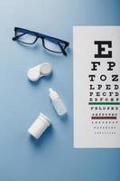 Glasses with Contact Lenses, drops and an Optometrist's Eye Test Chart On a Blue Background. photo