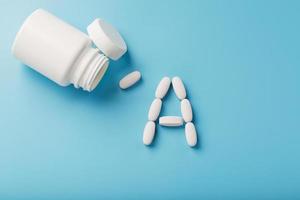 Vitamin A pills fell out of a white jar on a blue background. photo