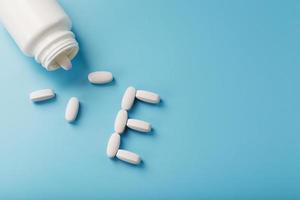 White capsules with vitamins in the form of E are poured from a jar on a blue background. photo