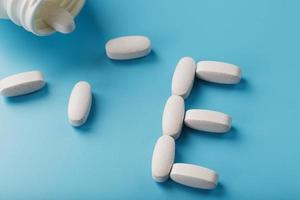 Vitamin E pills fell out of a white jar on a blue background. The letter E is an inscription. photo