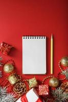 Christmas composition with notepad and a pencil for writing wishes with Christmas tree decorations on a red background. photo