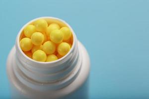 Vitamins of yellow color in the form of round dragees in a white jar on a blue background. photo