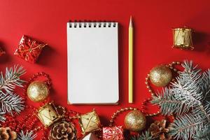 Notepad and pencil for writing wishes and gifts for the New Year and Christmas around the Christmas tree decorations on a red background. photo