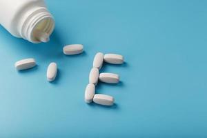 White capsules with vitamins in the form of E are poured from a jar on a blue background. photo