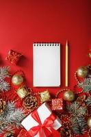 composición navideña con bloc de notas y un lápiz para escribir deseos con adornos de árboles de navidad sobre un fondo rojo. foto