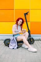 mujer usa un teléfono inteligente y un scooter eléctrico en el verano en la ciudad foto