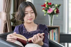 joven mujer asiática de pelo corto lee un libro en la sala de estar foto