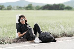 Woman sit with backpack hitchhiking along a road photo