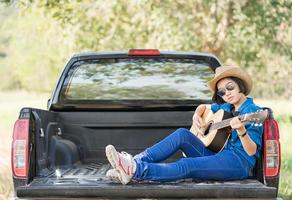 Woman wear hat and playing guitar on pickup truck photo