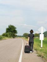 Woman with luggage hitchhiking along a road photo