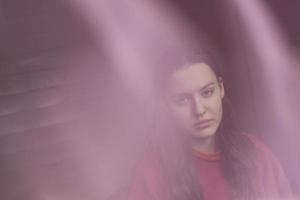 beautiful sad girl with long hair in a red pullover behind a pink veil, mental health concept photo