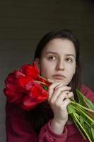 portrait of a girl in a red pullover with a bouquet of red tulips. The girl sits thinking with a bouquet of flowers. Love concept photo